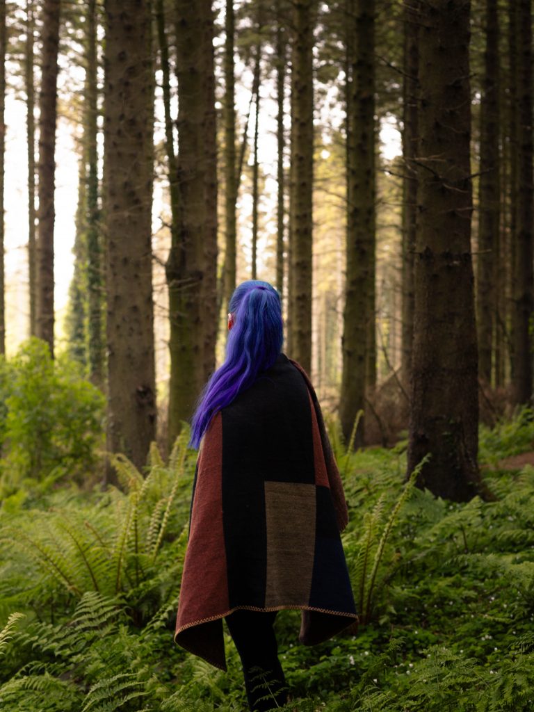 Shannon looking into the distance in the woods, with lighting from the left.